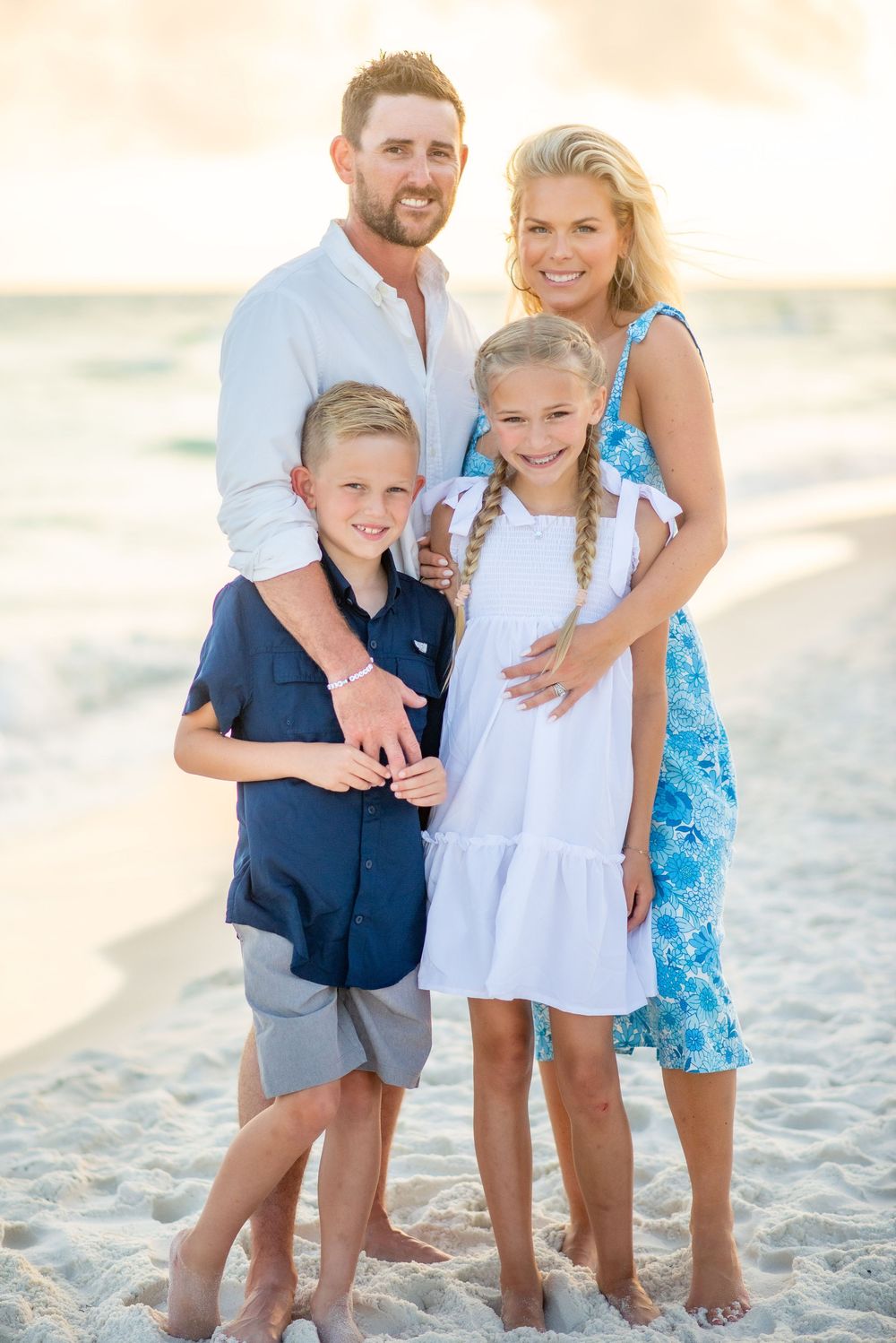 A family of four poses together on a sunny beach wearing coordinated casual beach attire.