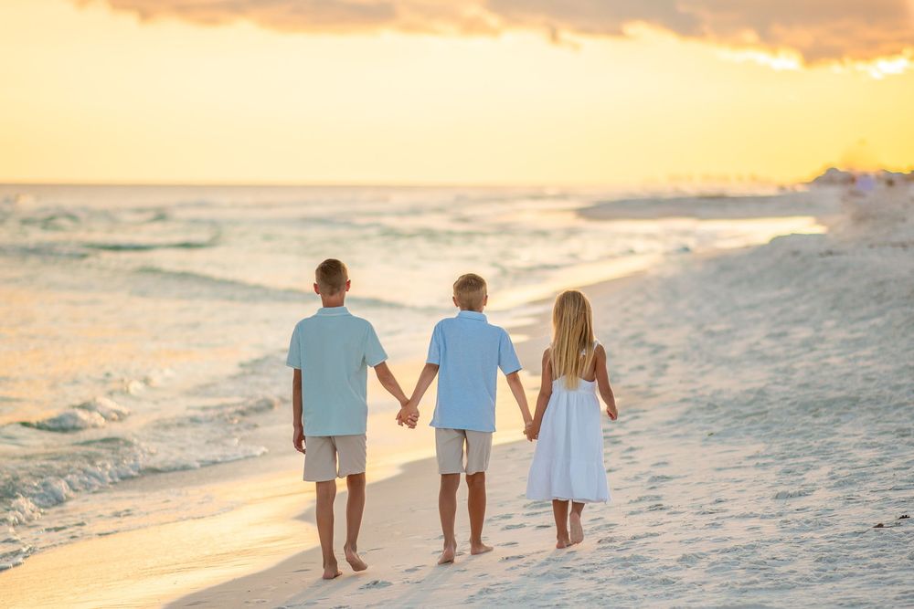 Three people walking hand in hand along the sandy beach at golden hour.