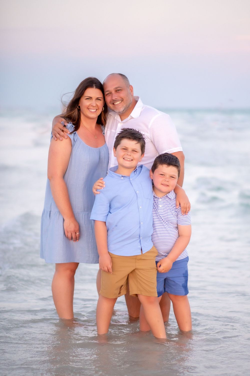 Family of four poses together at beach during sunset wearing coordinated blue and white outfits.