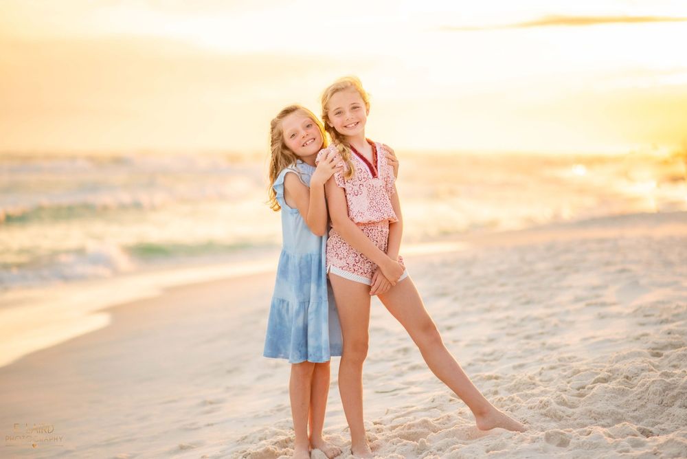 Two figures walk along a sandy beach at sunset casting long shadows on the golden sand.