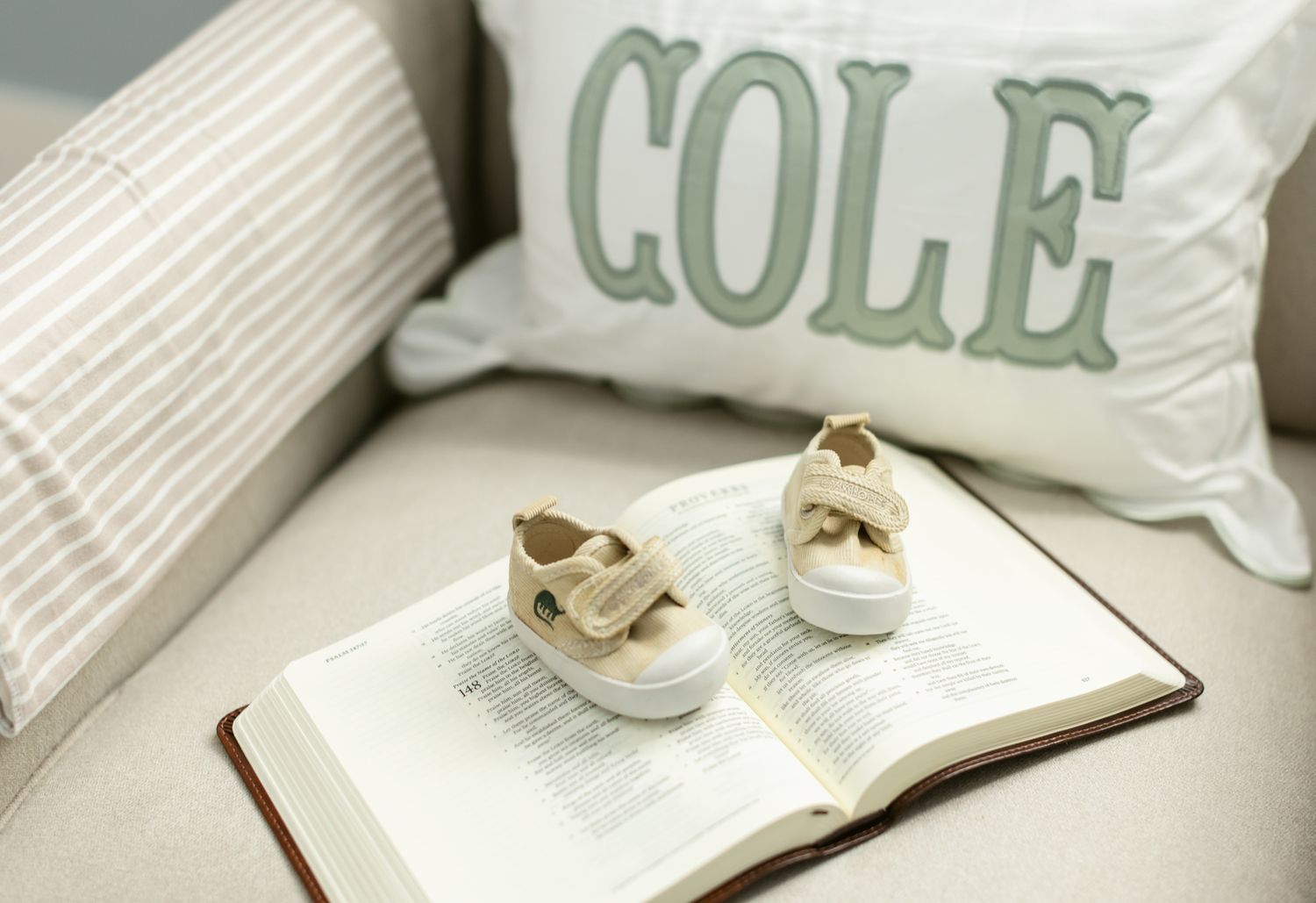 Newborn shoes rest on an open Bible in a crib with a pillow with the name Cole on it for newborn photos. Newburyport newborn photographer.