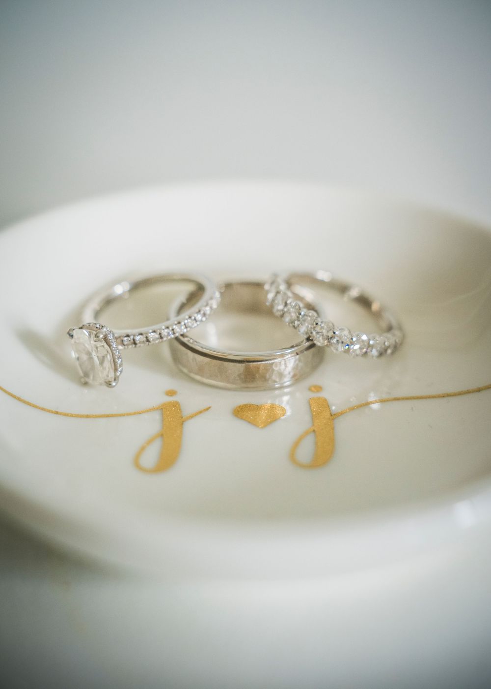 Three wedding rings displayed on a decorative white dish with gold initials.