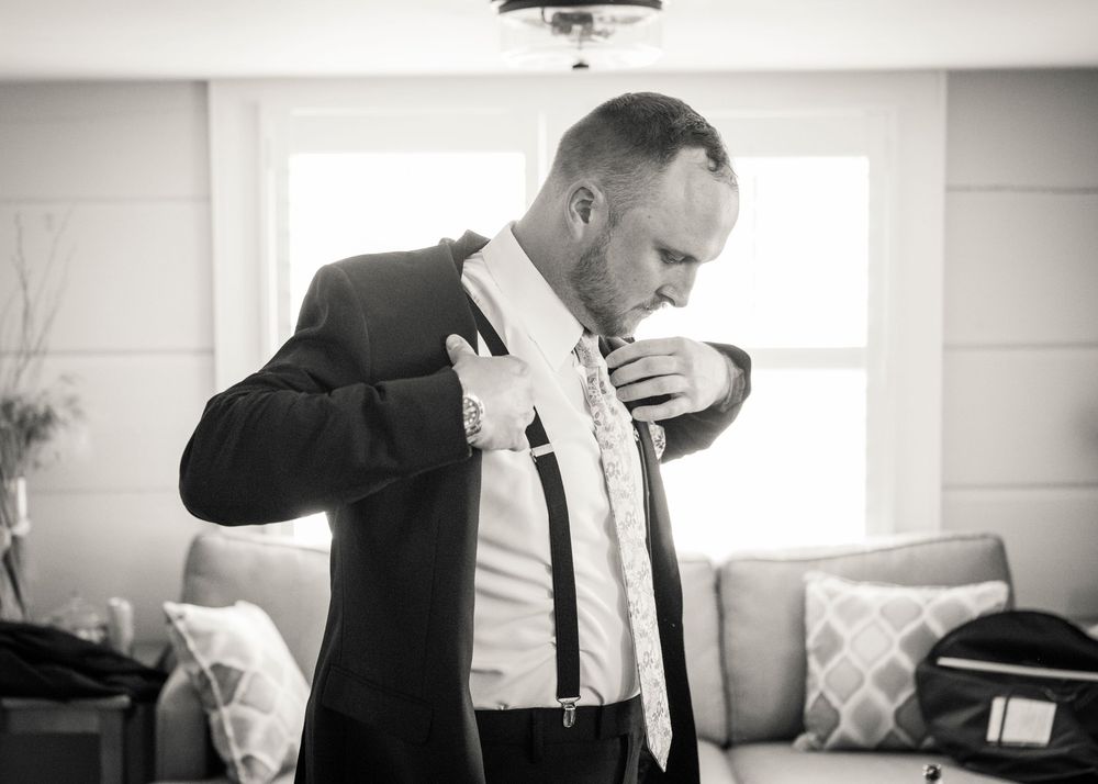 Groom in black suit adjusting boutonniere while getting ready for wedding ceremony.