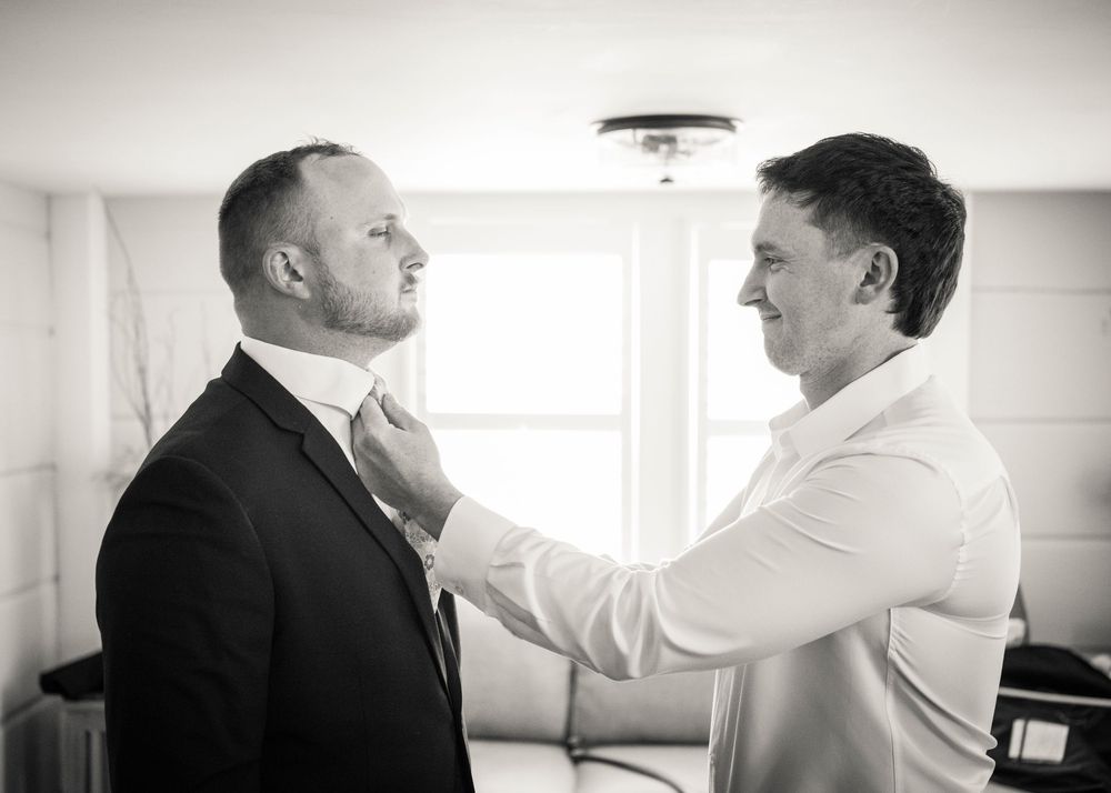 Black and white photo of groomsman adjusting grooms tie before wedding ceremony.