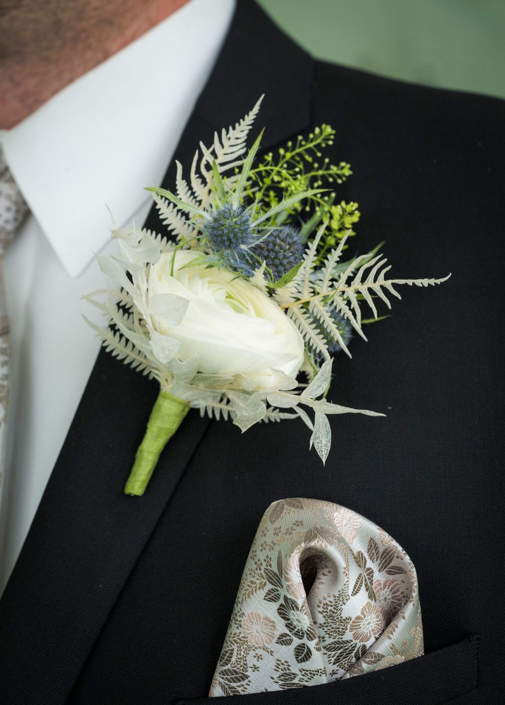Groom wearing black suit with white ranunculus and thistle boutonniere and floral pocket square.