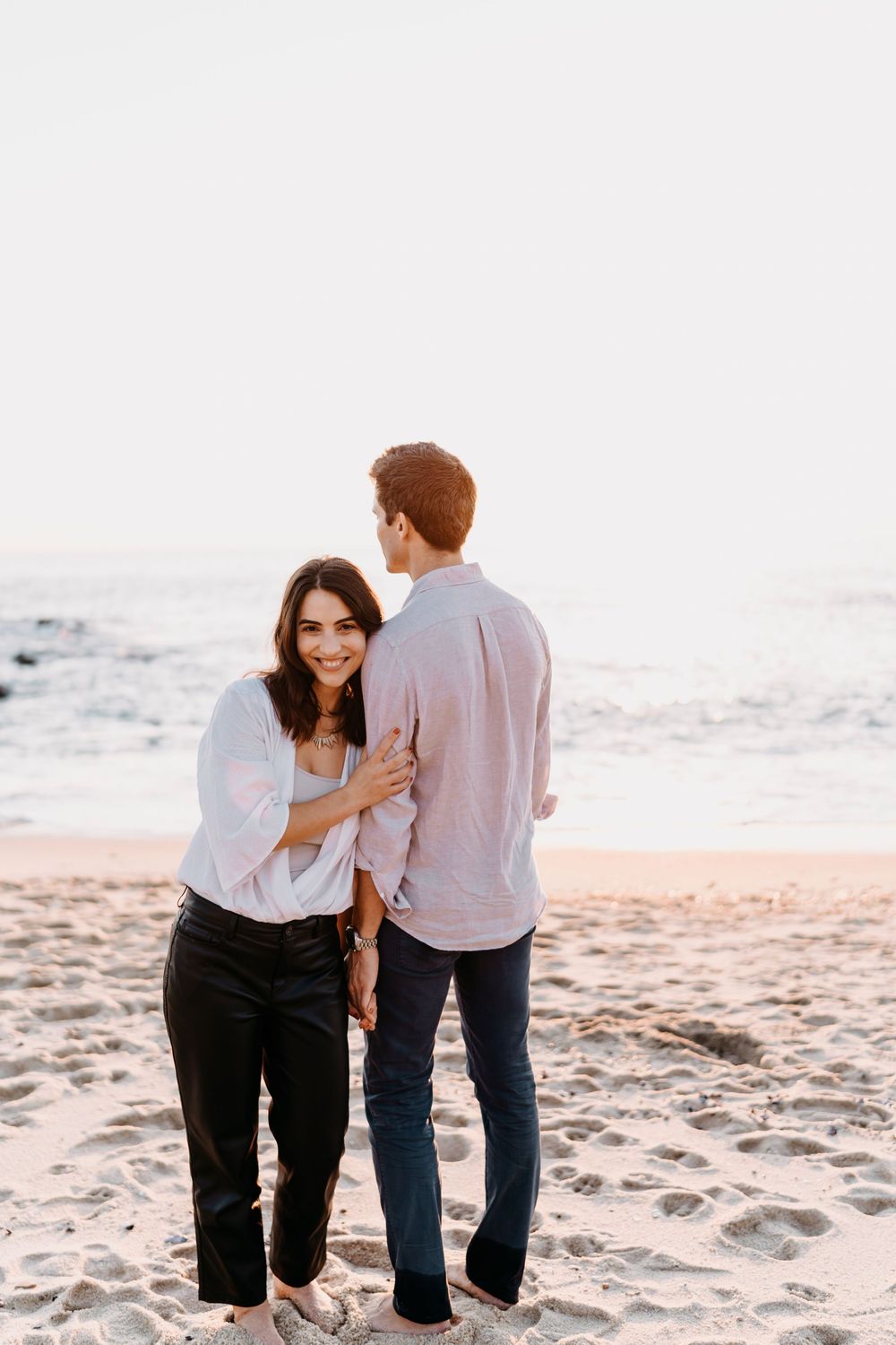A couple shares a romantic moment walking together on a sandy beach during sunset.