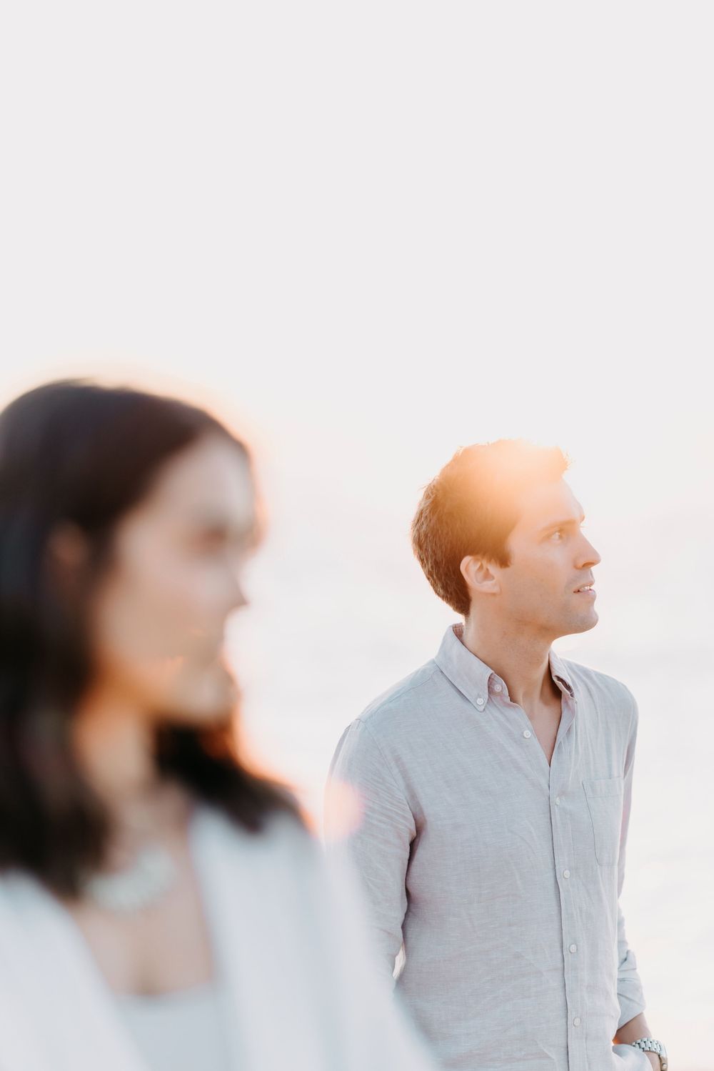Soft sunlit portrait of two people in white and light blue clothing standing against a bright background.