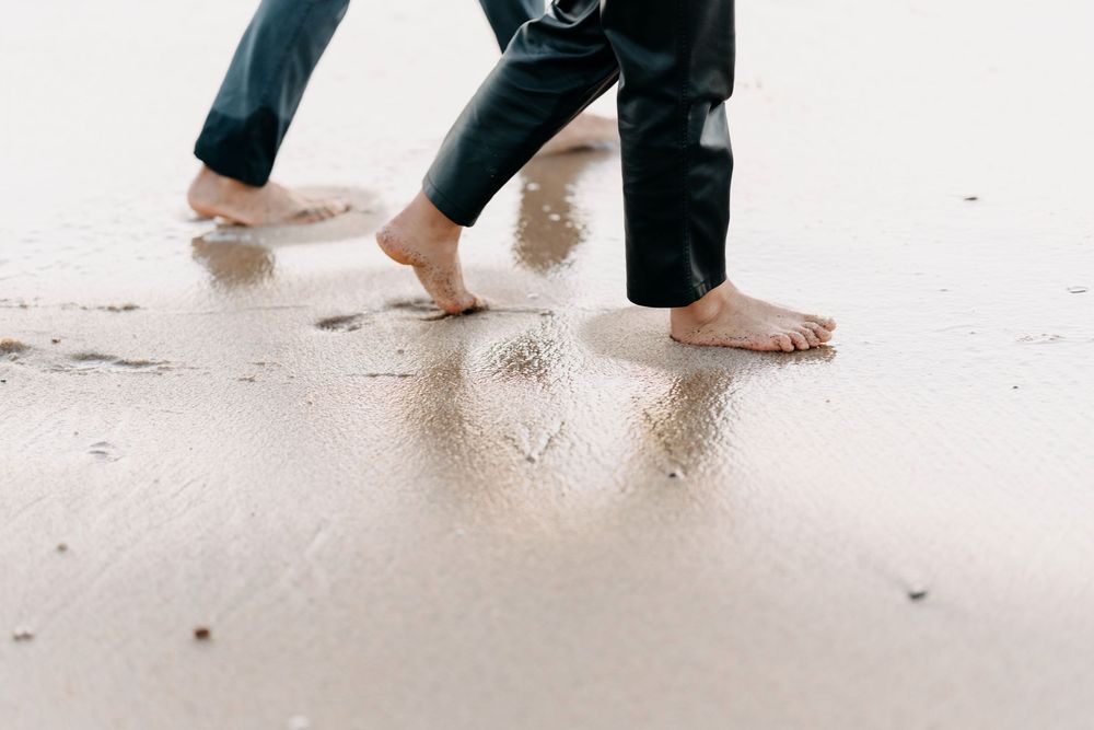 Bare feet walking on wet sand leaving footprints along a beach shoreline.