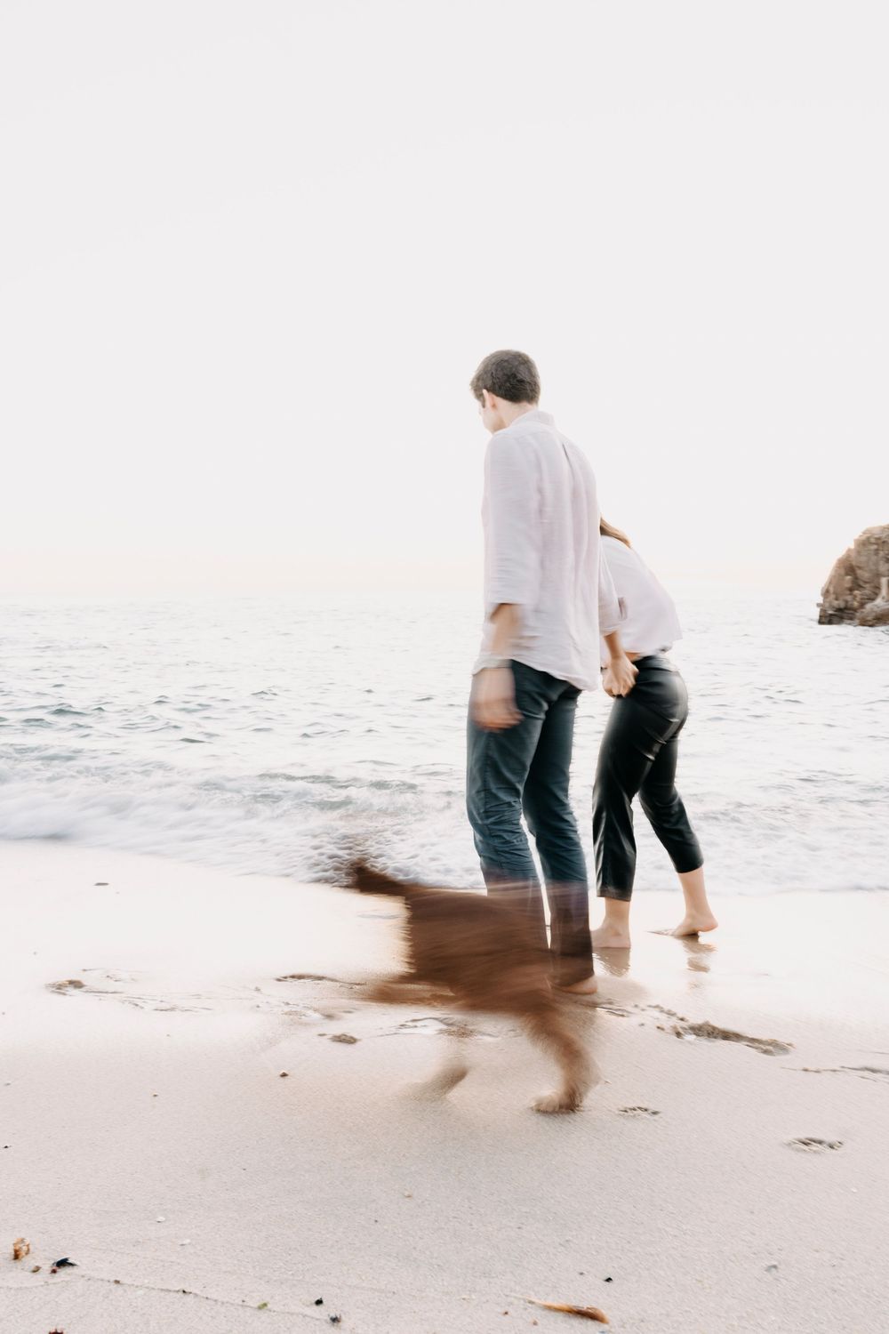 A couple walking along a misty beach shoreline shown in a series of four progressive photos.