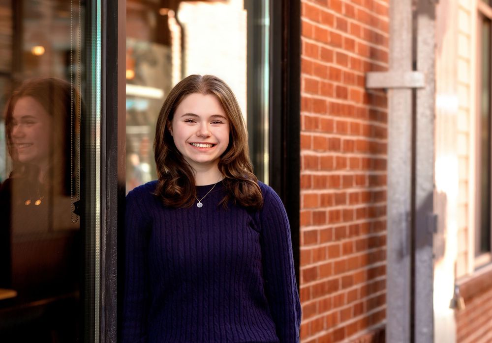 Senior girl standing by storefront window reflections in downtown Concord NH senior photos.