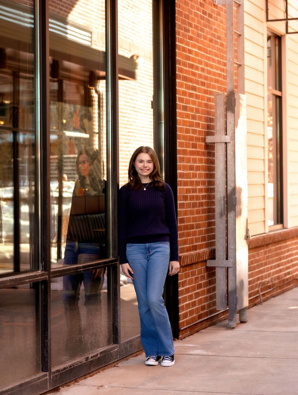 Senior girl standing along brick storefront in downtown Concord NH golden hour portrait.