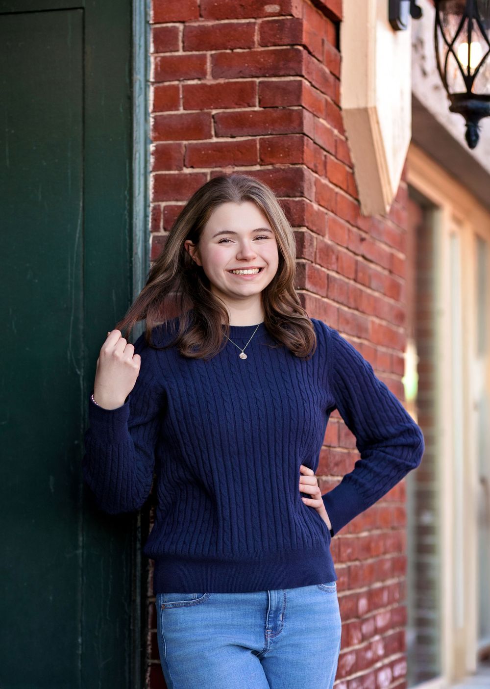 Senior girl portrait by red brick wall in downtown Concord NH during winter senior photo session.