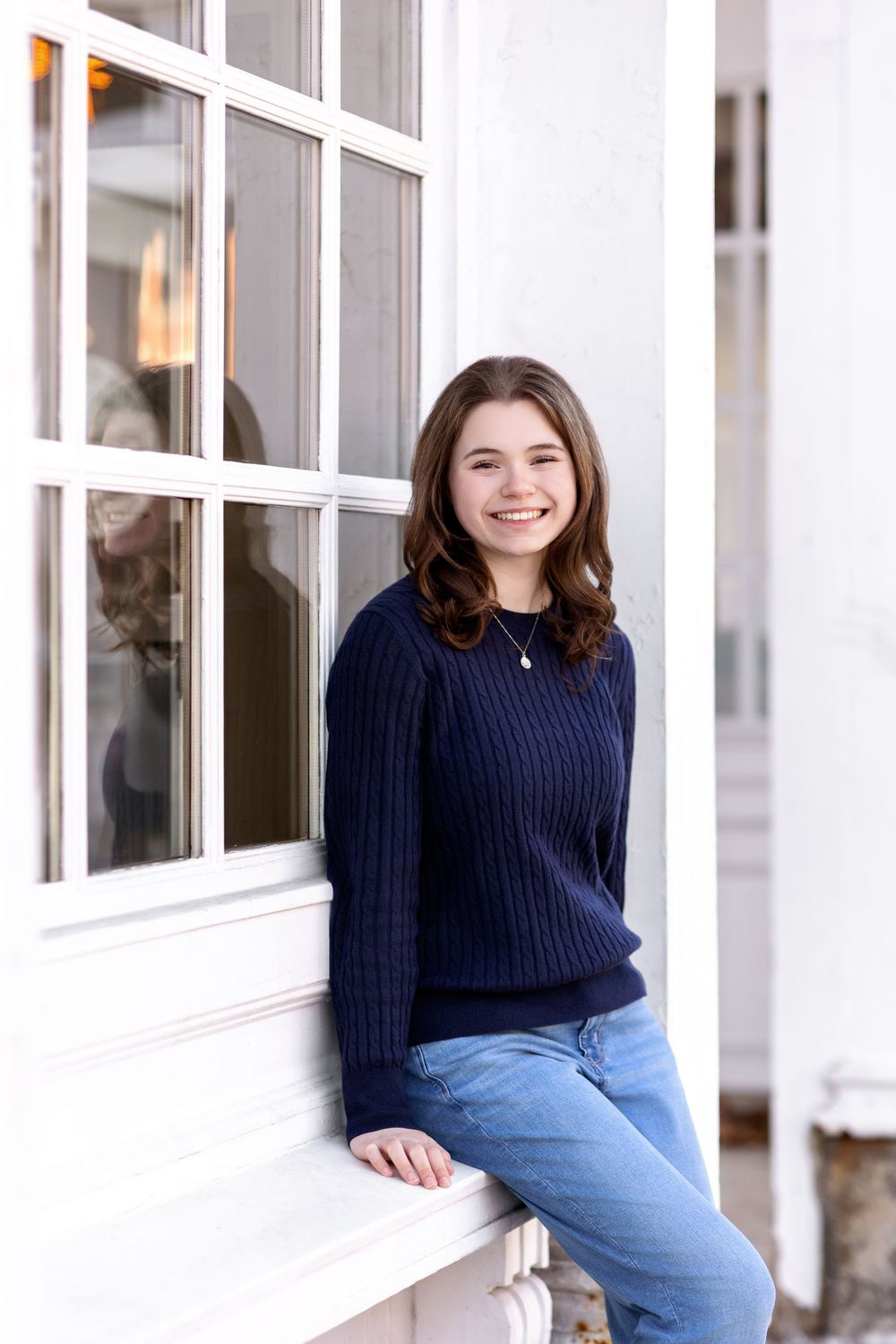 Senior girl sitting by white storefront window in downtown Concord NH senior session.