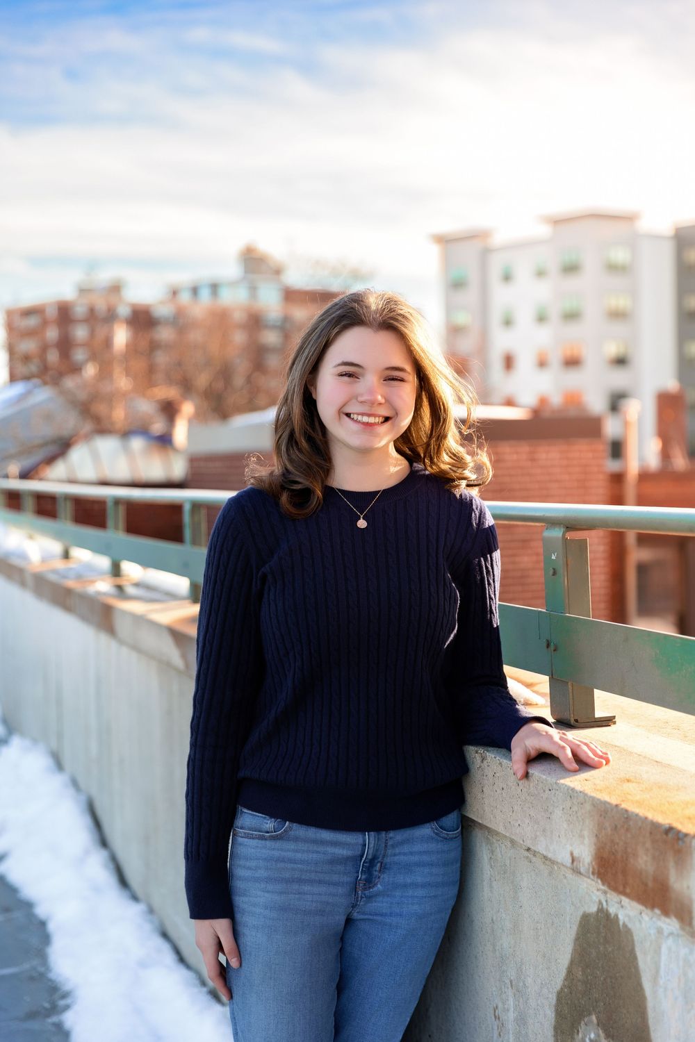 Senior girl leaning on rooftop railing overlooking downtown Concord NH buildings and skyline.