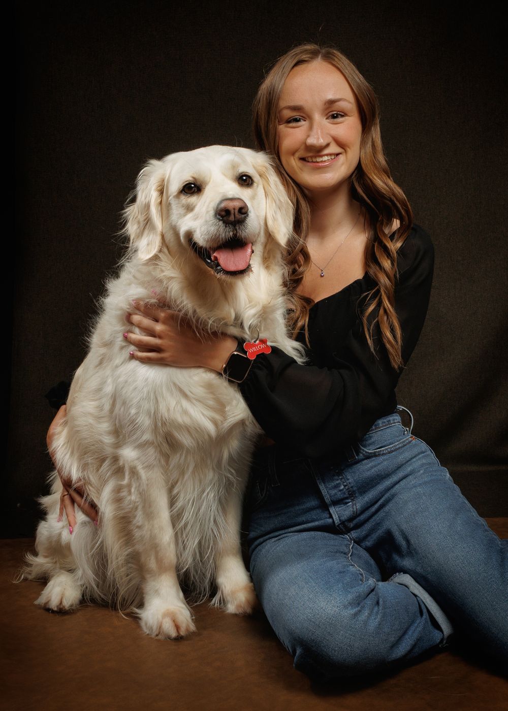 Young woman smiling and hugging a fluffy white Golden Retriever dog in a professional studio portrait.