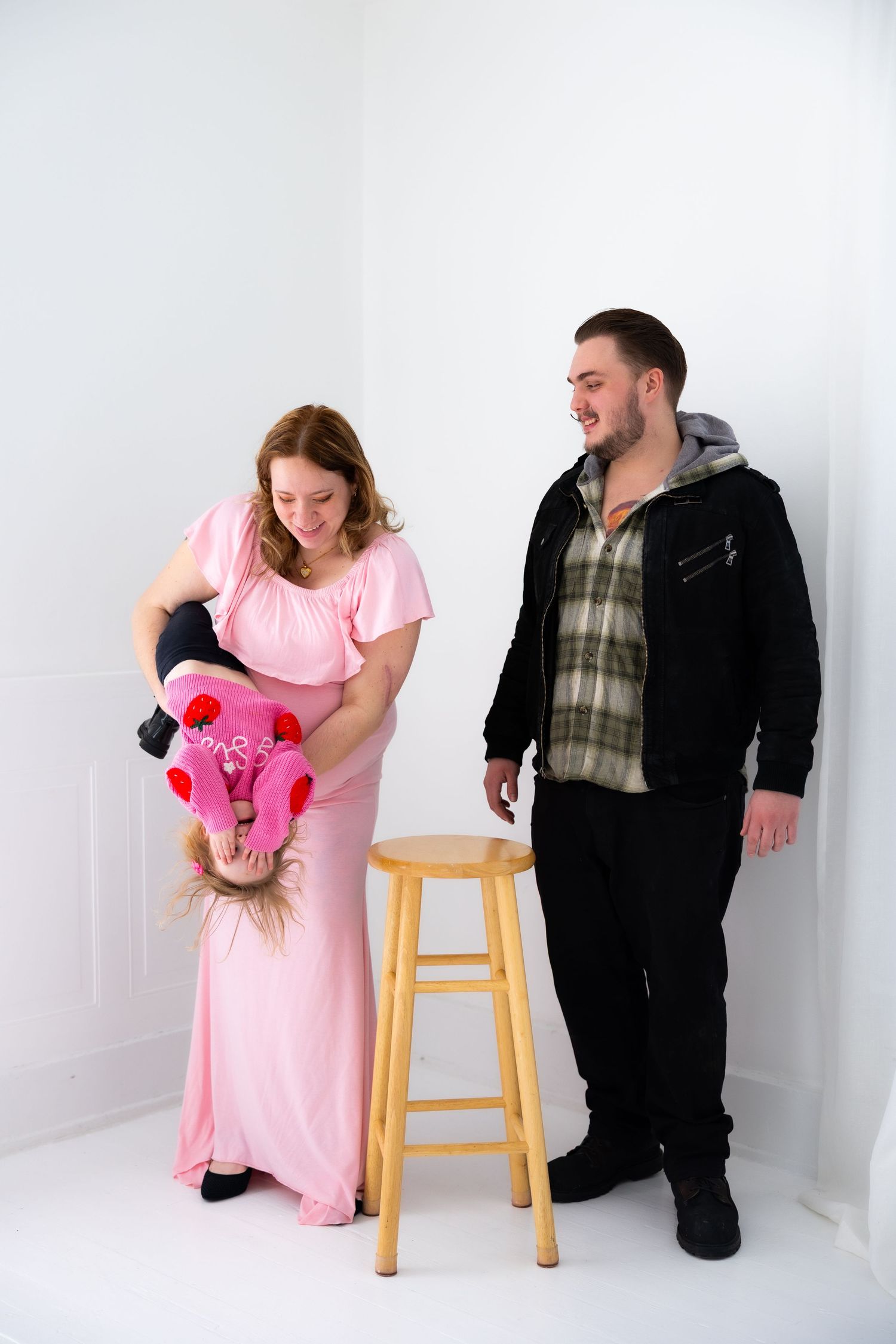 A couple in contrasting pink and black outfits poses playfully in a series of studio shots with a wooden stool.