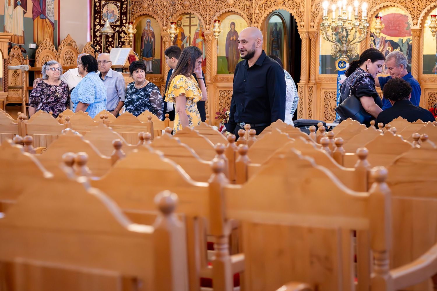 People gathered inside an ornate Orthodox church with wooden pews and golden iconostasis during a religious service.
