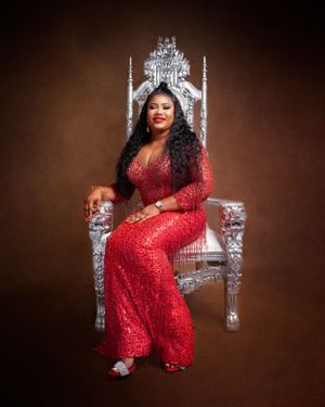 Glamorous photo shoot featuring sparkly red gown and ornate silver throne against dark brown backdrop.