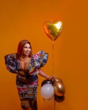 Celebratory portrait session with balloons against vibrant orange background.