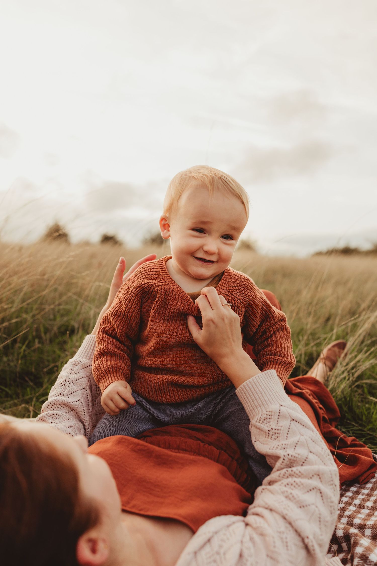 Family enjoying tender moments together in a sunlit meadow during golden hour, with trees in the background.