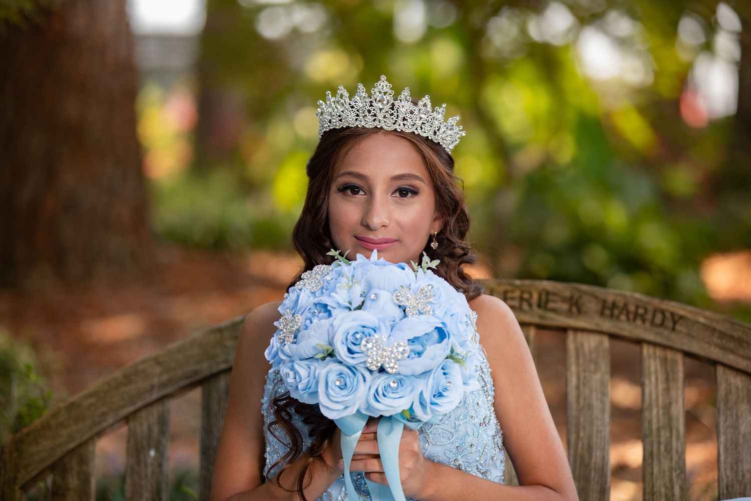 Expectant woman in flowing mauve gown and floral crown poses elegantly against neutral backdrop in maternity photo.