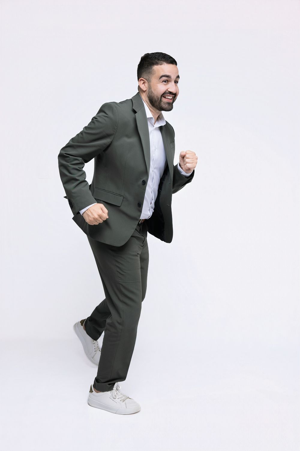 Energetic person in a gray suit and sneakers striking a playful running pose against white background.