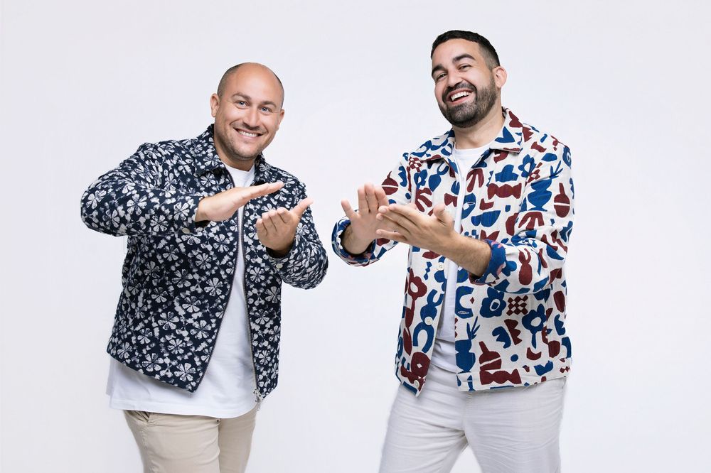 Two men in patterned shirts posing playfully against white background.