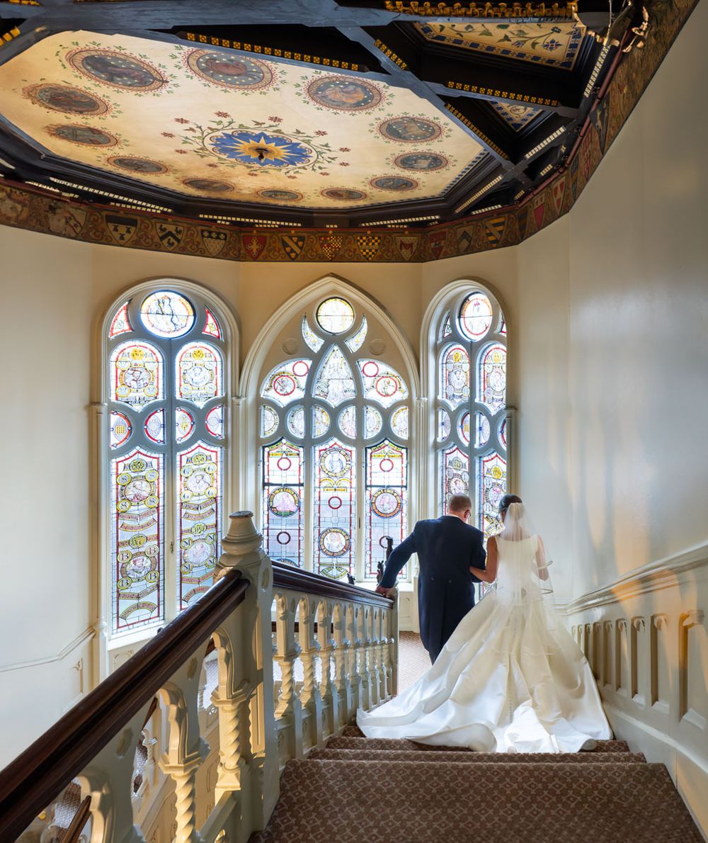 Father walks bride down grand staircase in country mansion
