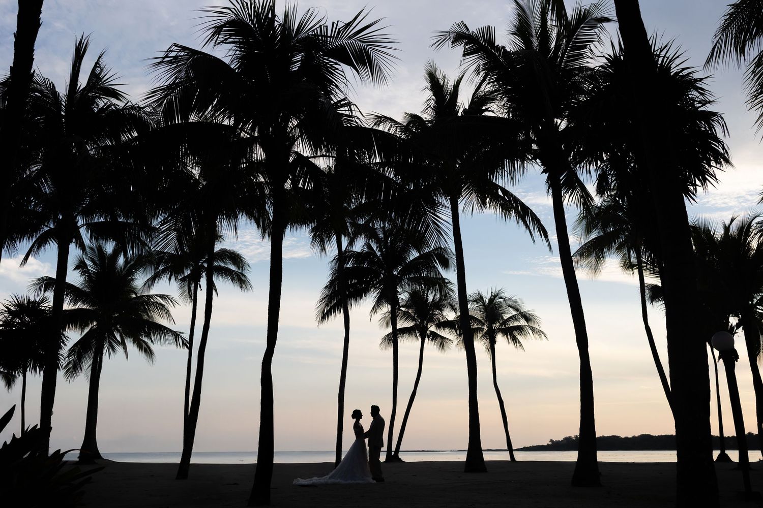 Romantic couple embraces on a sunny beach at golden hour with stunning lens flare lighting effects.
