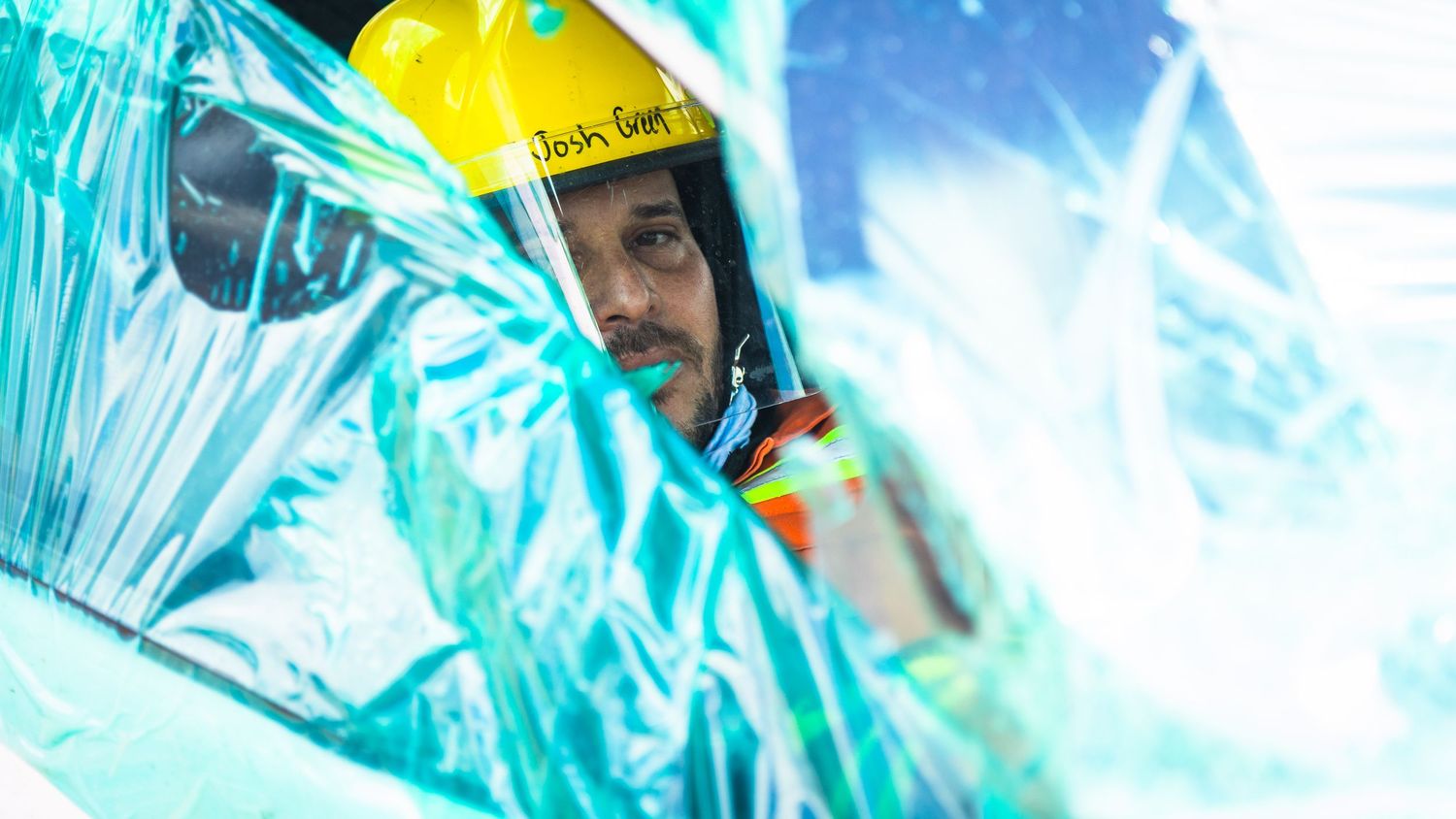 A person in protective gear works with glowing blue liquid in a scientific laboratory setting.