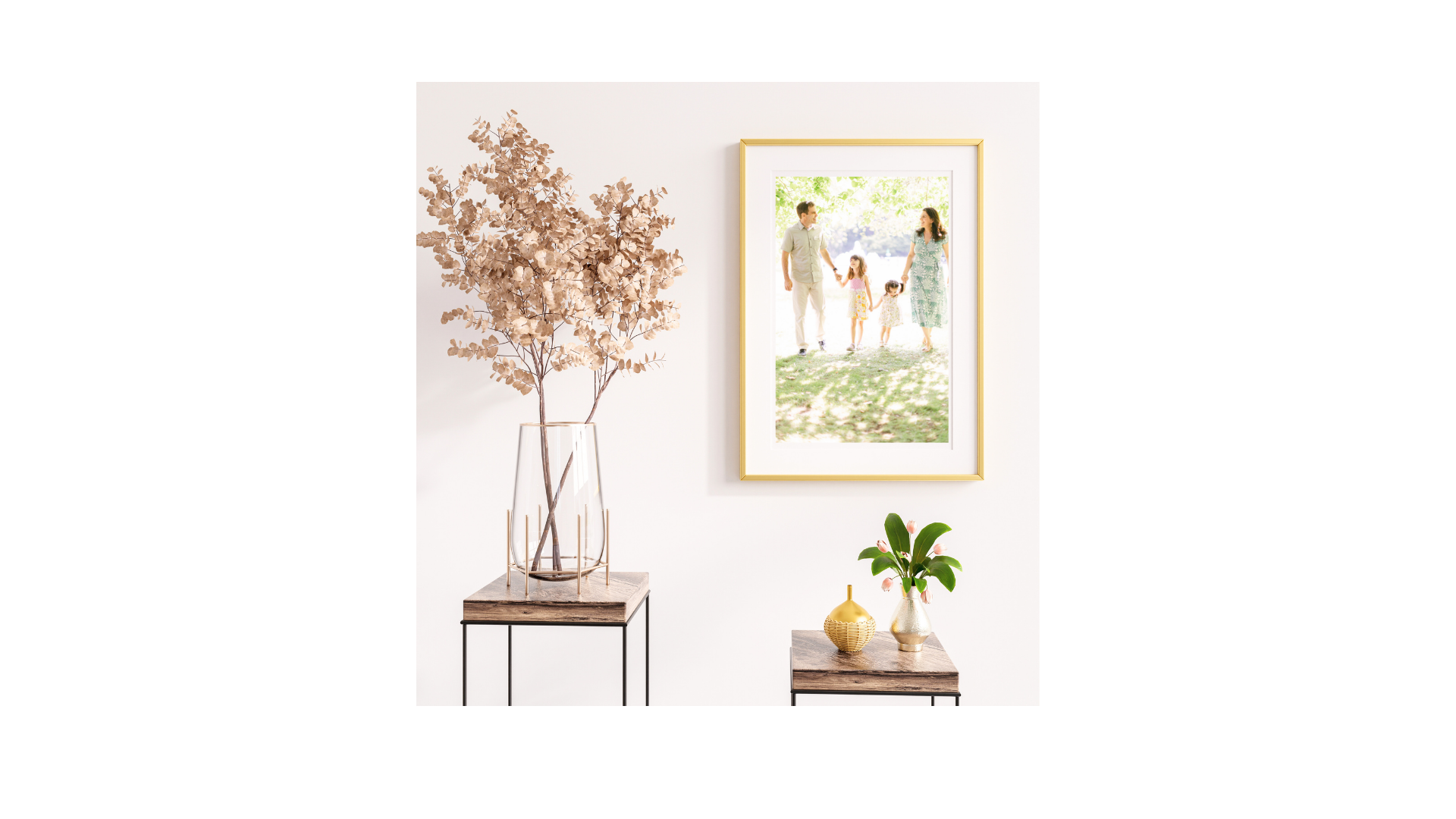 A framed artwork hanging above wooden console tables decorated with dried botanicals.