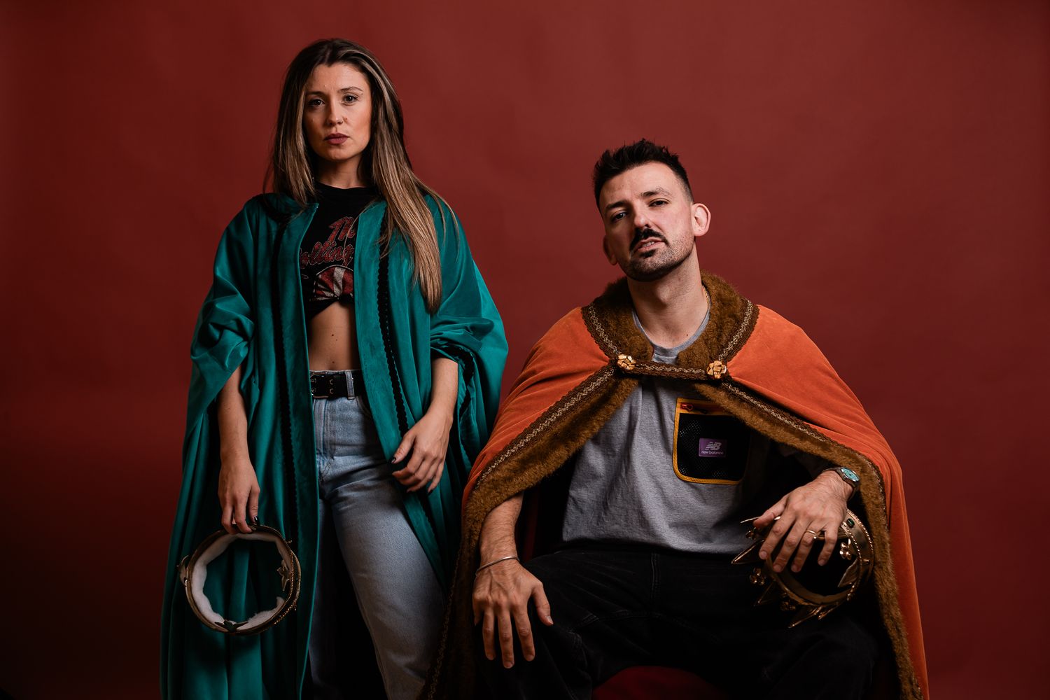 Two performers in colorful outfits posing against a red backdrop for a stylish promotional photo.
