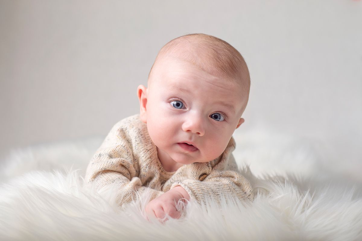 four month baby boy on belly in tummy time position looks up for milestone session in studio session Baltimore, Ontario*