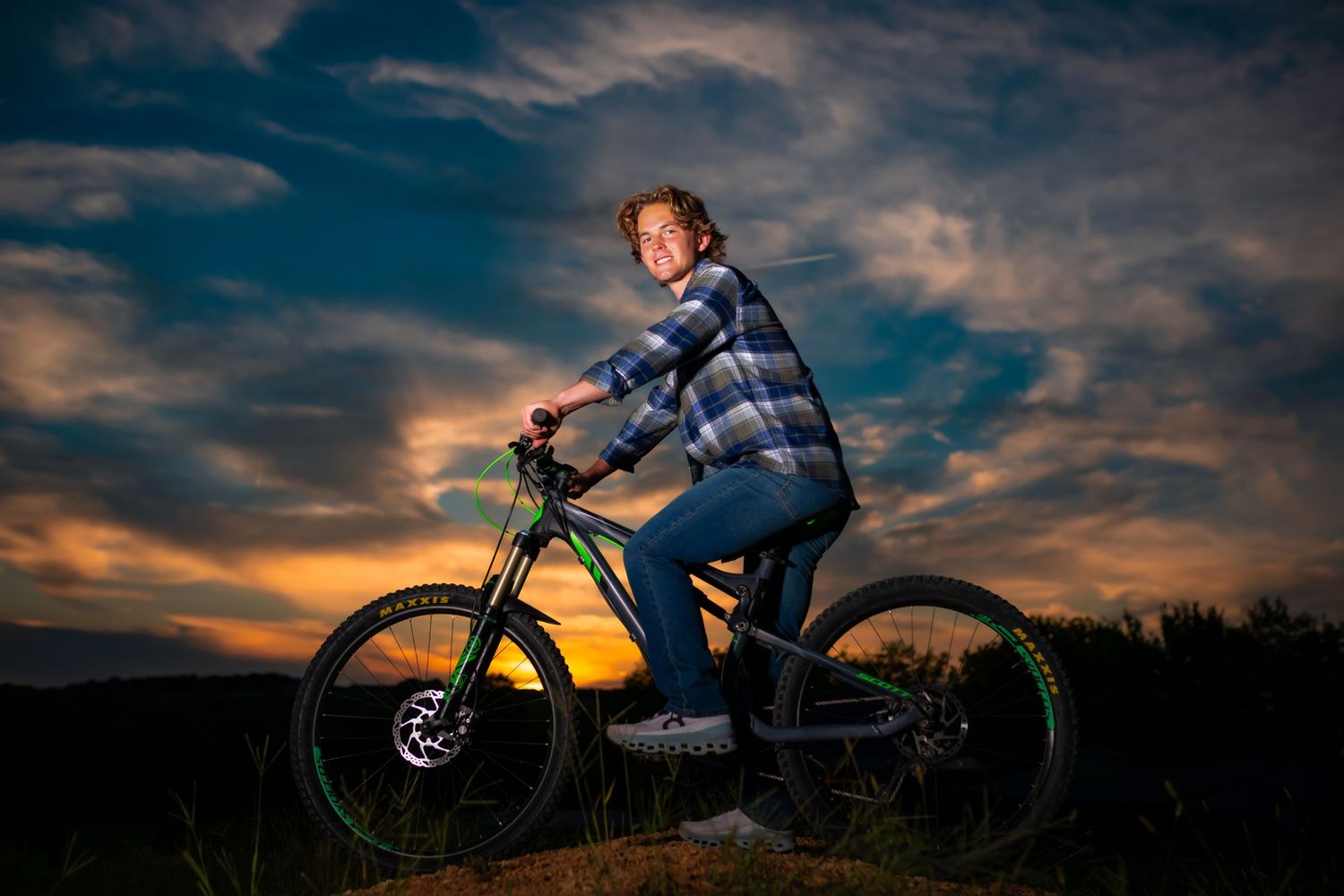 Mountain biker poses on bike against dramatic sunset sky.