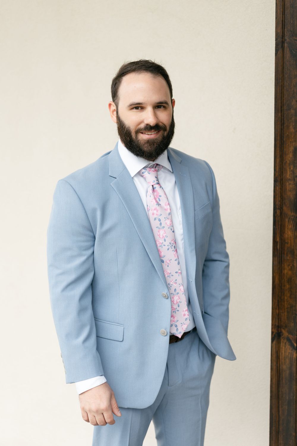 Formal portrait of a groom wearing a light blue suit with floral pink tie.