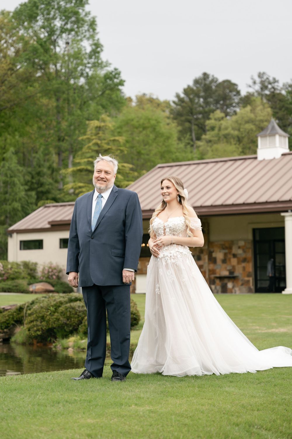 A wedding moment captured on manicured grounds with stone building and pond in background.
