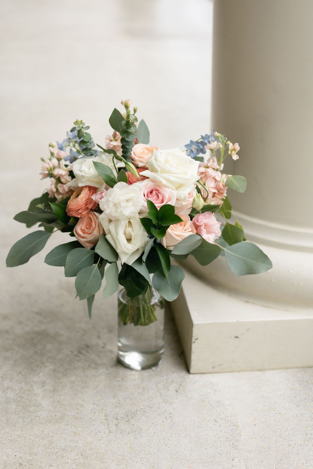 Elegant wedding bouquet with pink and white roses and eucalyptus leaves in a glass vase.