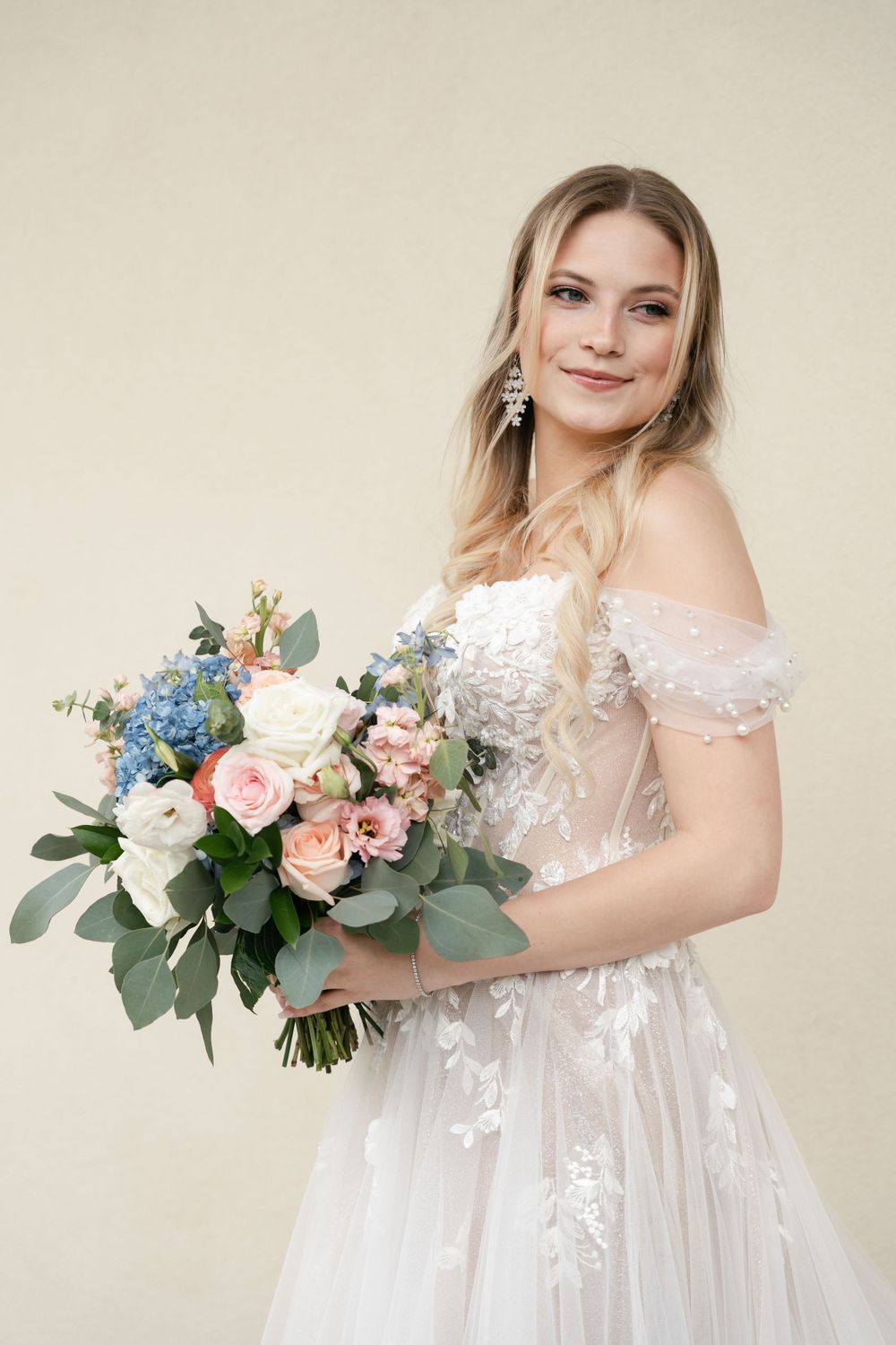Studio portrait of a bride in a delicate lace gown holding a pastel bouquet.
