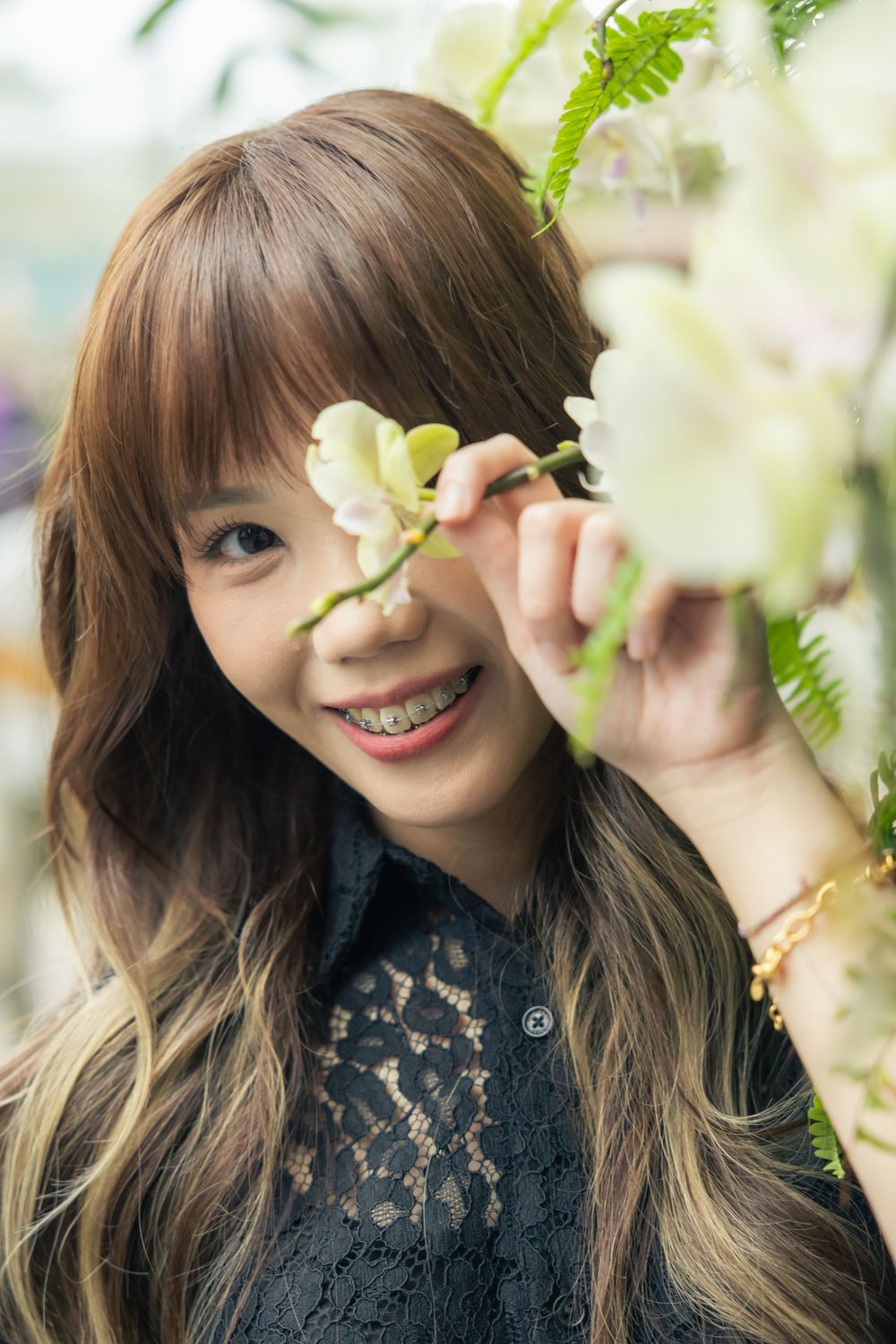A person playfully poses with orchids while wearing a black lace dress in a garden setting.