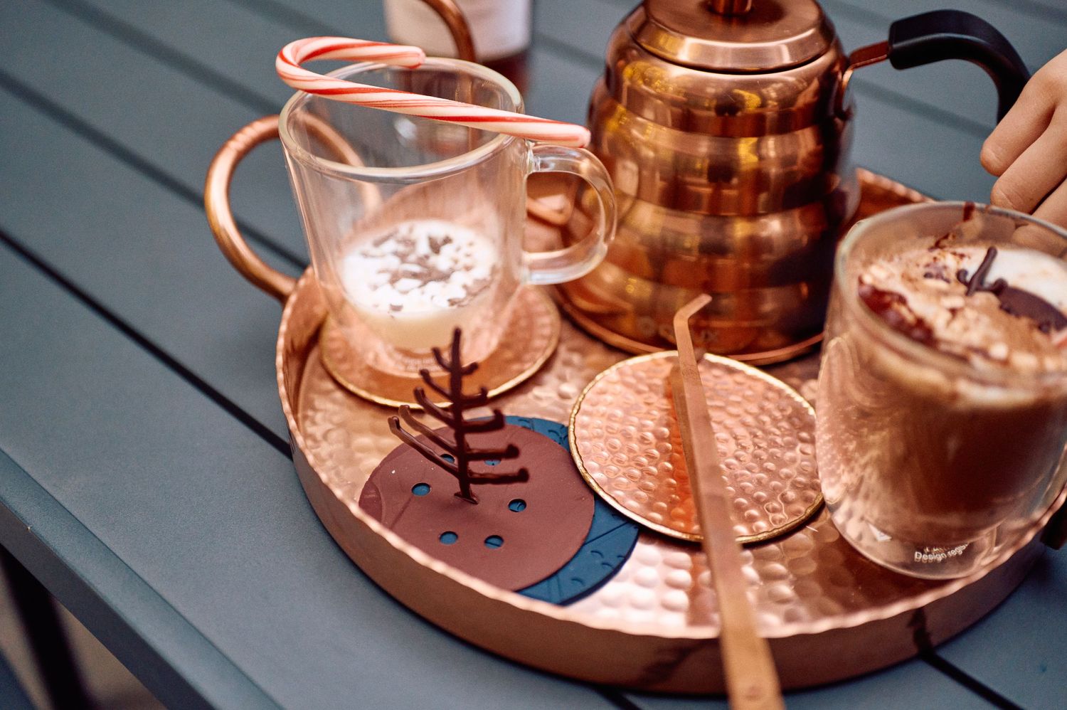 Copper kettle and glasses filled with coffee drinks served on a hammered copper tray with elegant garnishes.