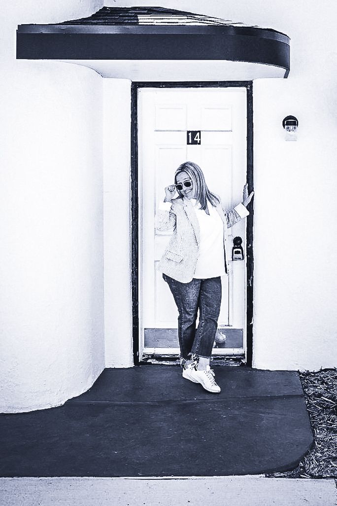 Casual lifestyle portrait of woman posing in doorway with black and white effect.