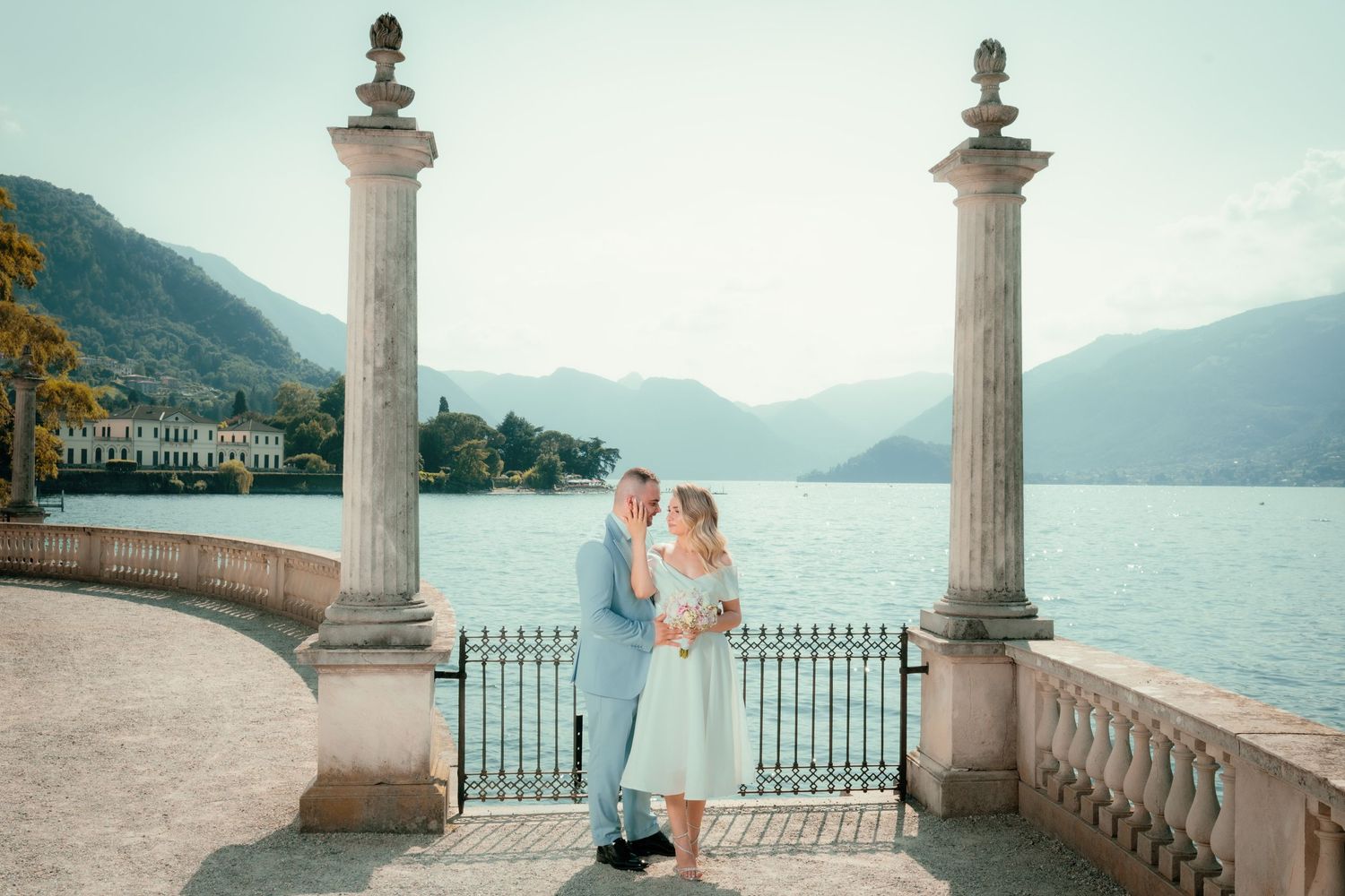 A romantic moment captured between pillars overlooking Lake Como in Italy with mountains and villas in background.