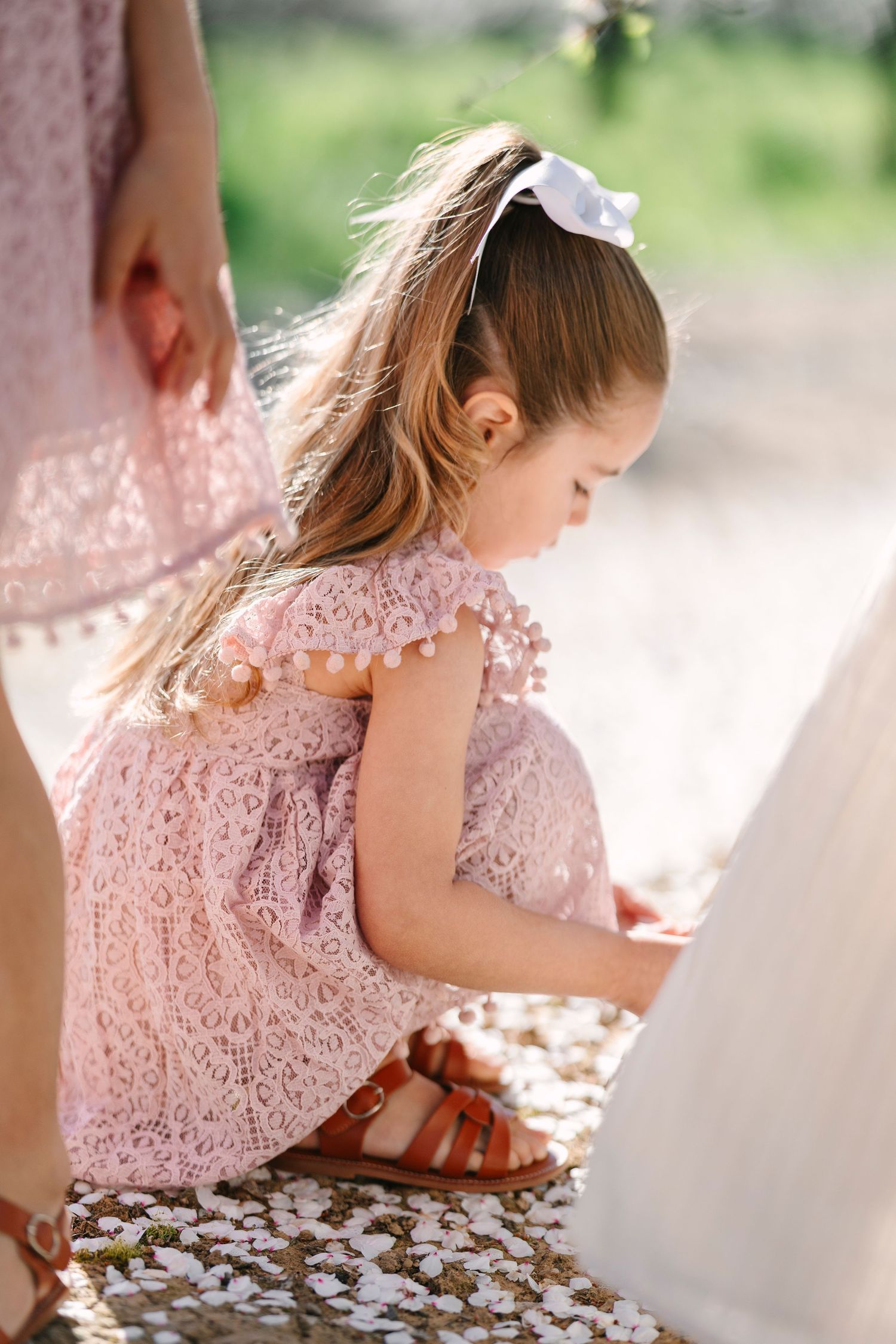 Child in pink lace dress sitting among cherry blossom petals.