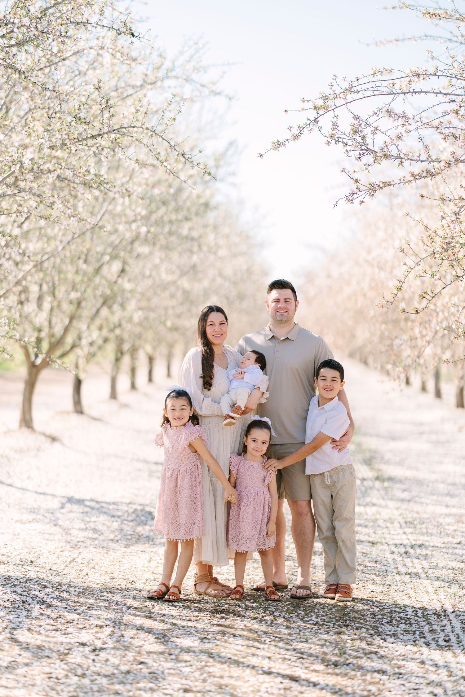 Family photo session in a blooming cherry blossom orchard during spring.