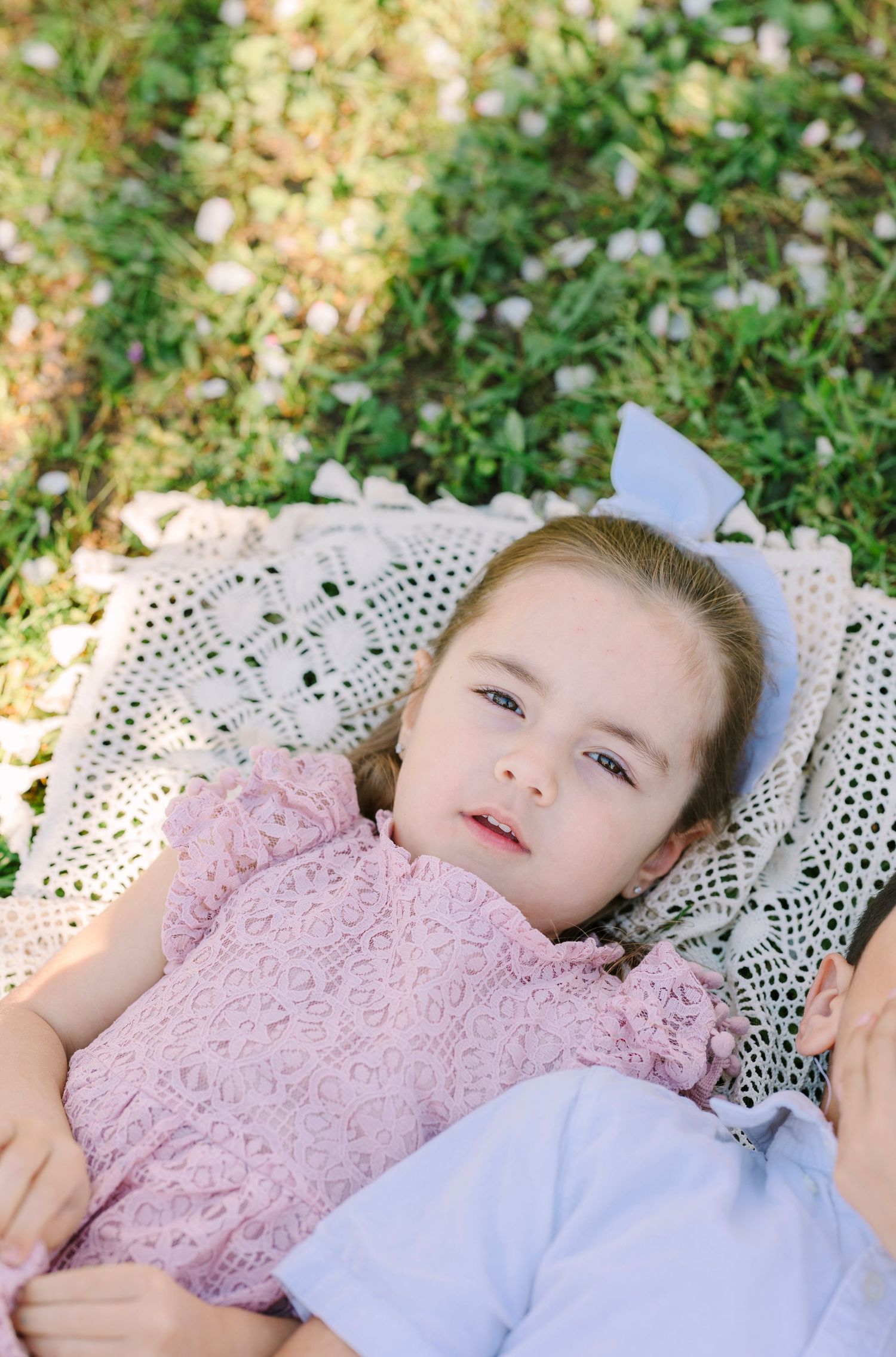 Person in pink lace dress lying on white lace blanket in garden setting.