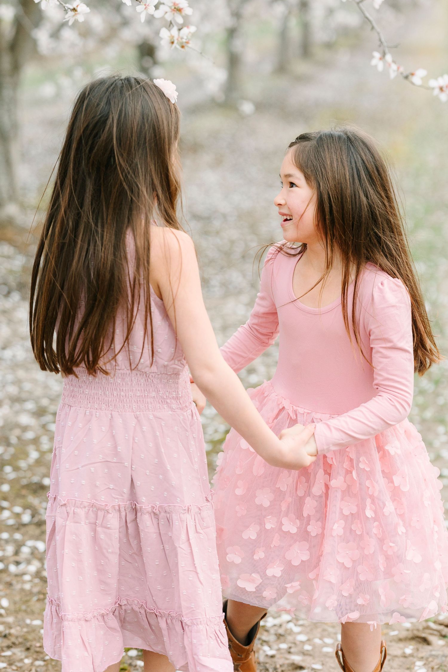 Children in matching pink dresses playing under cherry blossom trees.