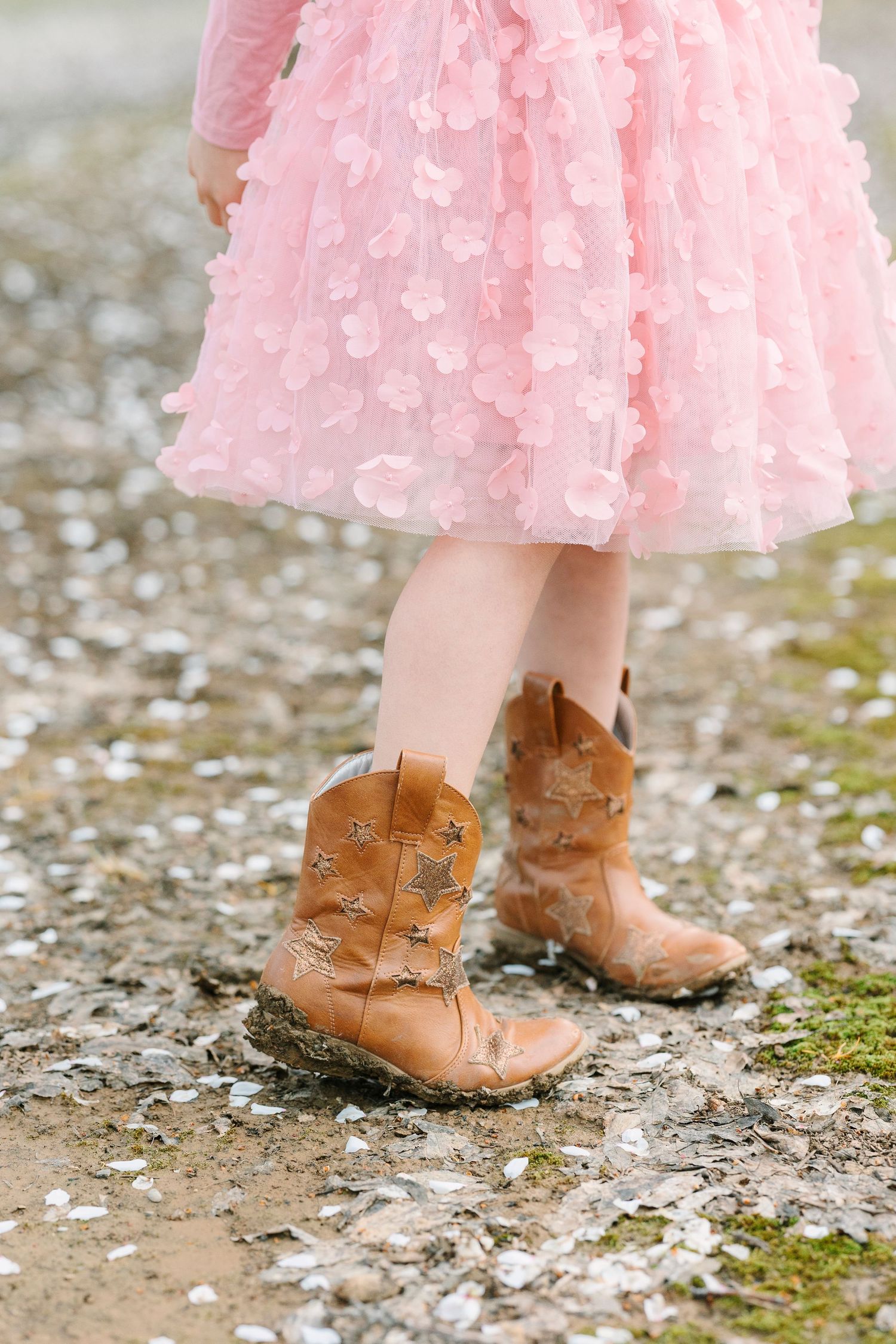 Brown leather boots paired with a flowing pink dress against cherry blossom petals.