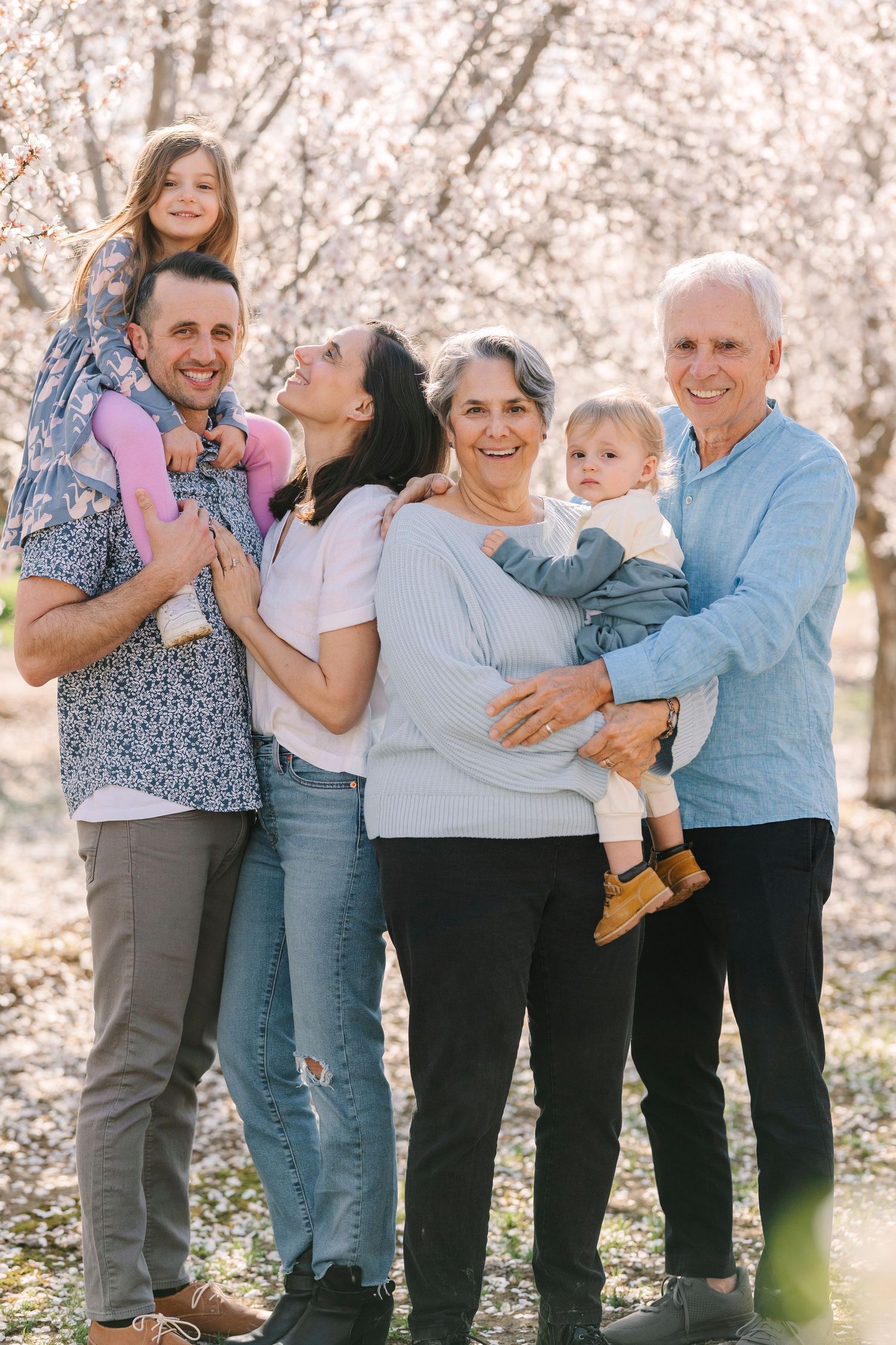 Multi-generational family sharing laughs and embraces in spring orchard setting.