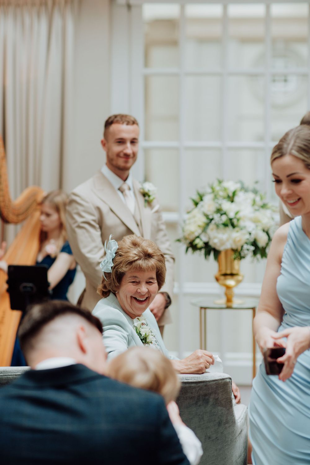 Wedding guests share a joyful moment during a reception with a harp player and floral arrangements.