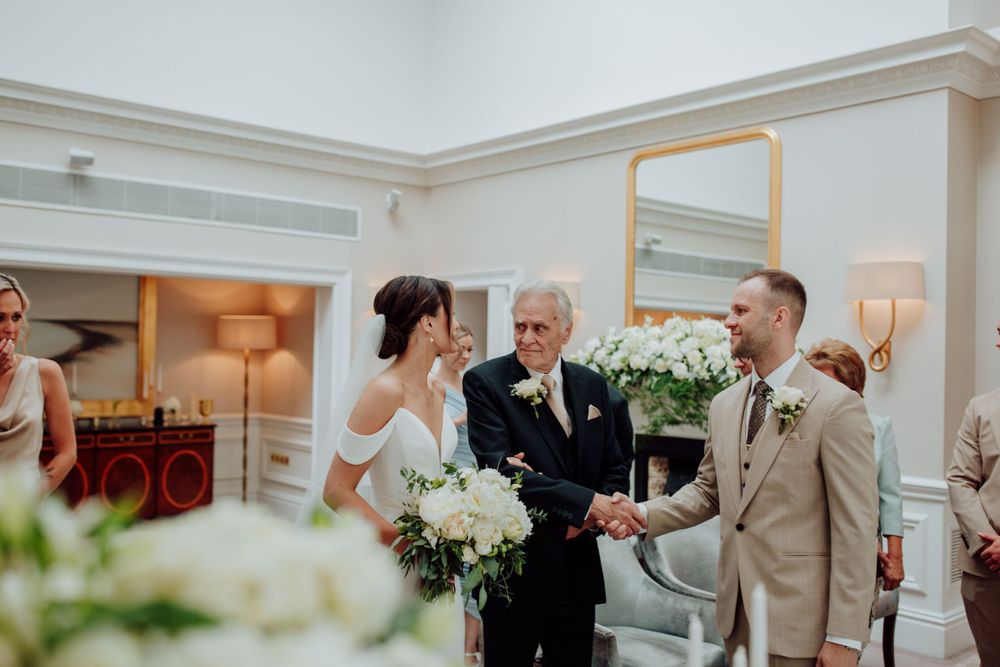 An intimate indoor wedding ceremony with white floral arrangements and warm lighting in an elegant room.